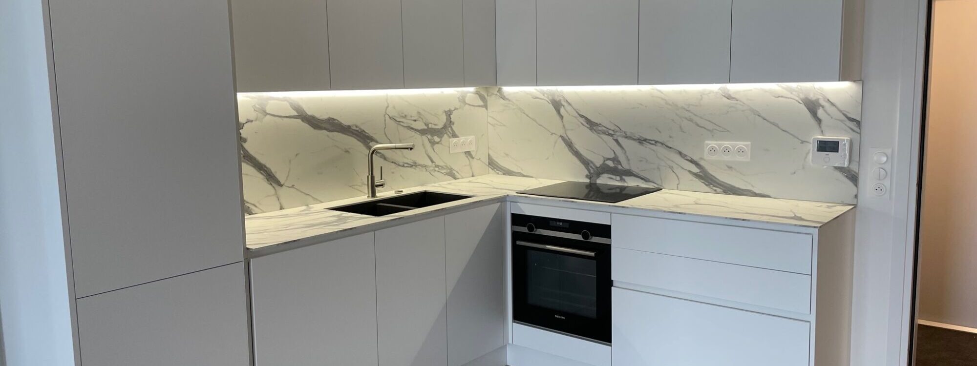 Cuisine blanche version XXL, caisson ht 78 cm, profil plat laqu&eacute; blanc mat en m&eacute;tal et plan de travail Compact ultra mat finition marbr&eacute; &eacute;p 1 cm avec cr&eacute;dences toute hauteur. Poign&eacute;e verticale en m&eacute;tal laqu&eacute; blanche pour les portes du frigo. Bischwiller
