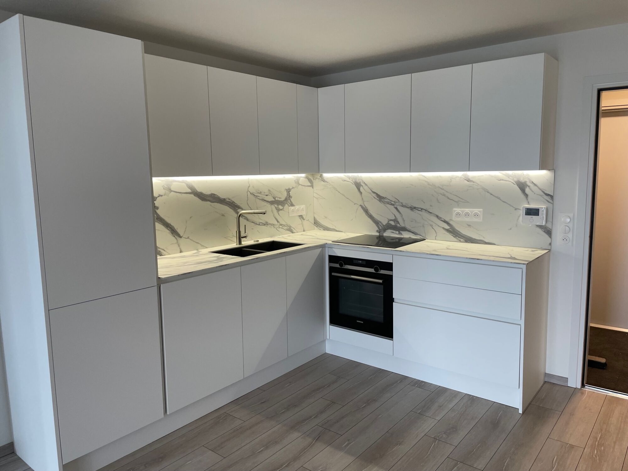 Cuisine blanche version XXL, caisson ht 78 cm, profil plat laqu&eacute; blanc mat en m&eacute;tal et plan de travail Compact ultra mat finition marbr&eacute; &eacute;p 1 cm avec cr&eacute;dences toute hauteur. Poign&eacute;e verticale en m&eacute;tal laqu&eacute; blanche pour les portes du frigo. Bischwiller